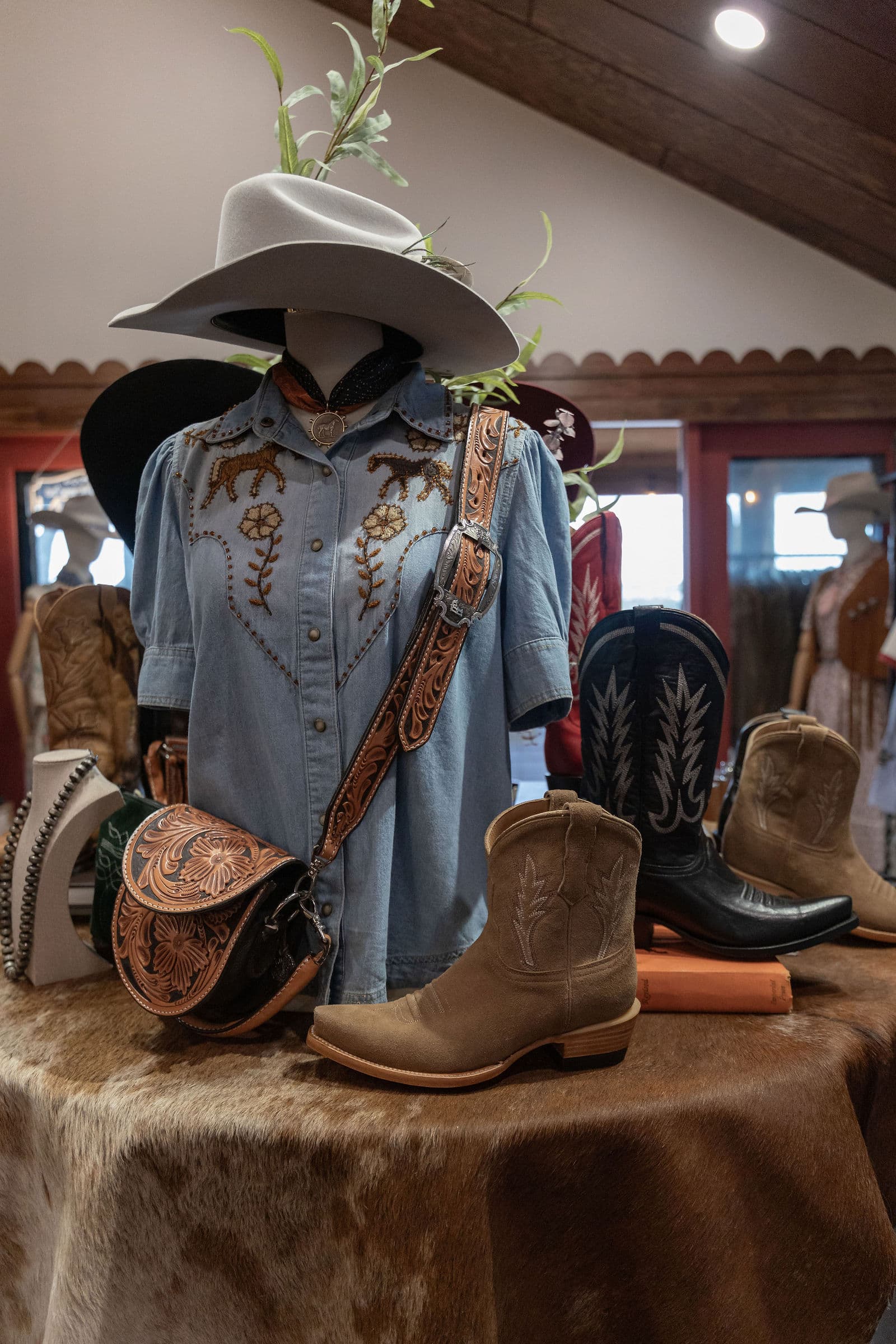 Western product display at the Billie Jean Boots launch in Austin: embroidered denim, hat, tooled leather bag, and boots on a cowhide rug