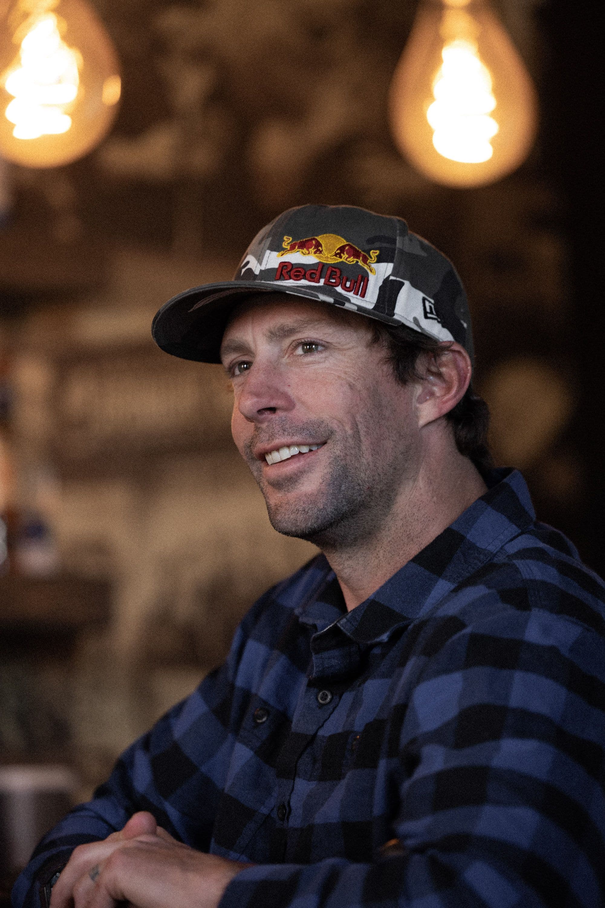 Bar-side conversation at a rustic branded lounge, warm overhead lights and bottles on shelves