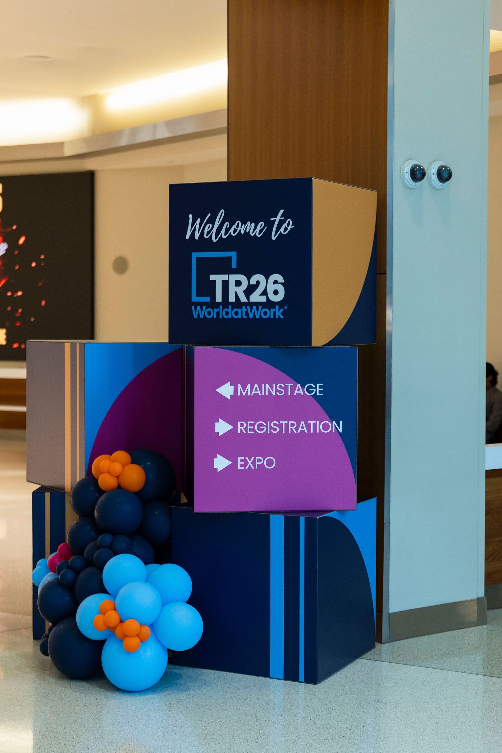 Branded wayfinding cubes and balloons at World at Work Total Rewards 2026 in Austin, pointing to mainstage, registration, and expo