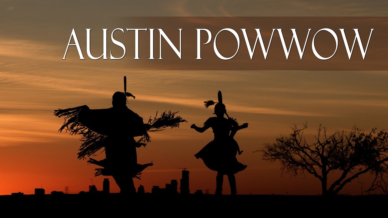 Two dancers in regalia at sunset during Austin Powwow, Austin skyline on the horizon