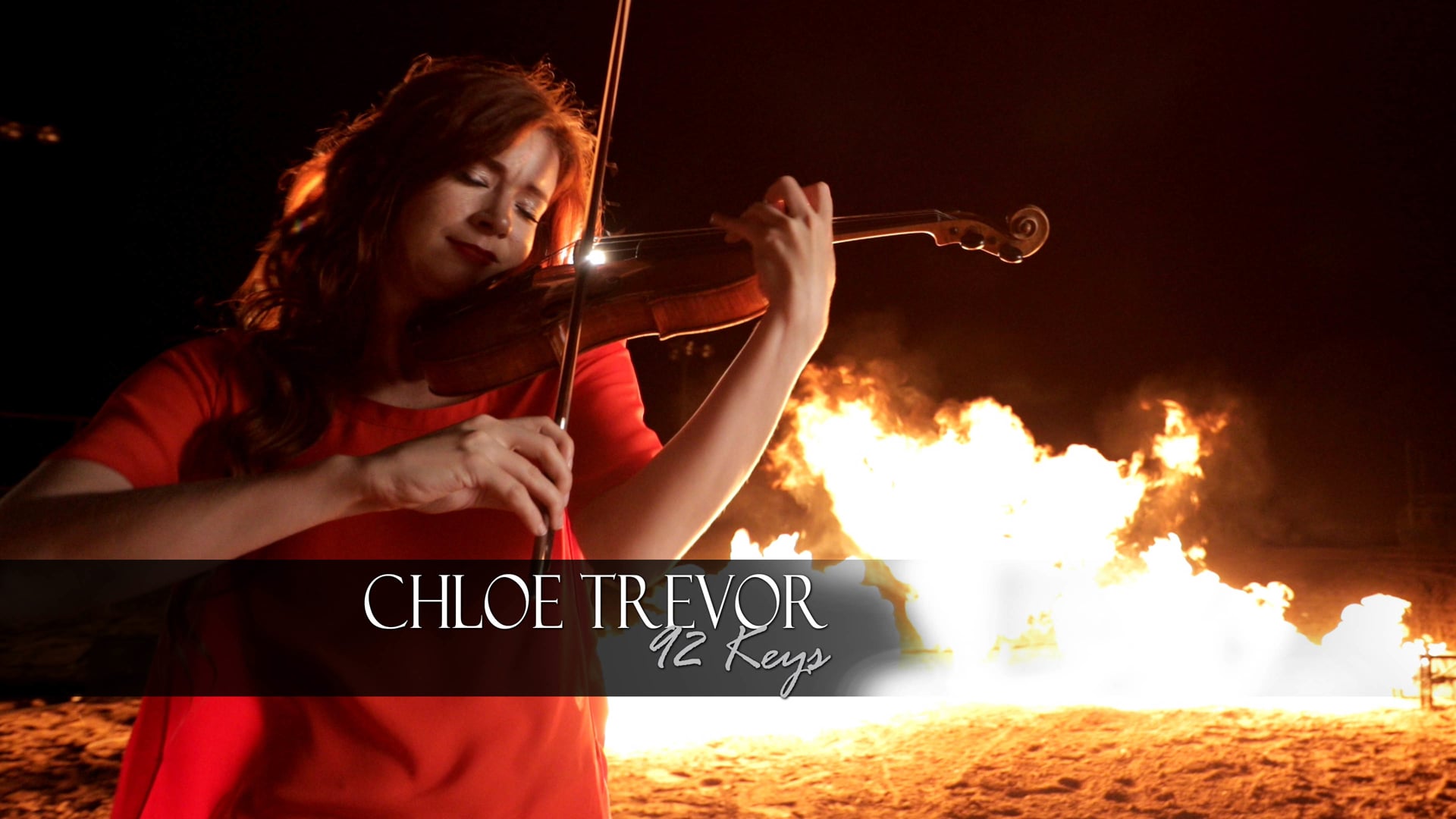 Violinist Chloe Trevor playing outdoors at night with a large fire behind her